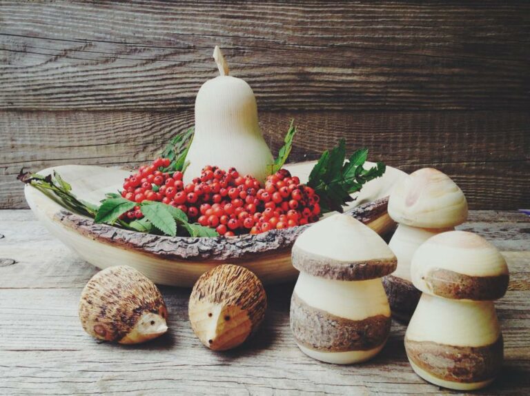 eine Holzschale, gefüllt mit reifen Ebereschenbeeren, davor zwei kleine Igel und Pilze aus Holz
